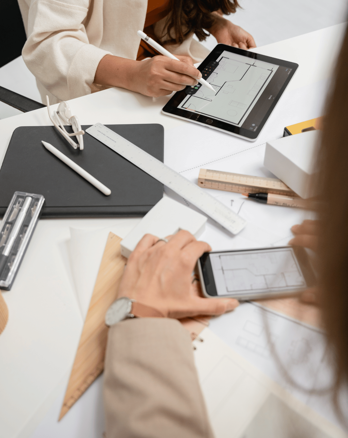 Deux personnes travaillant sur des plans et des dessins techniques sur une tablette et un smartphone dans un bureau d'études.