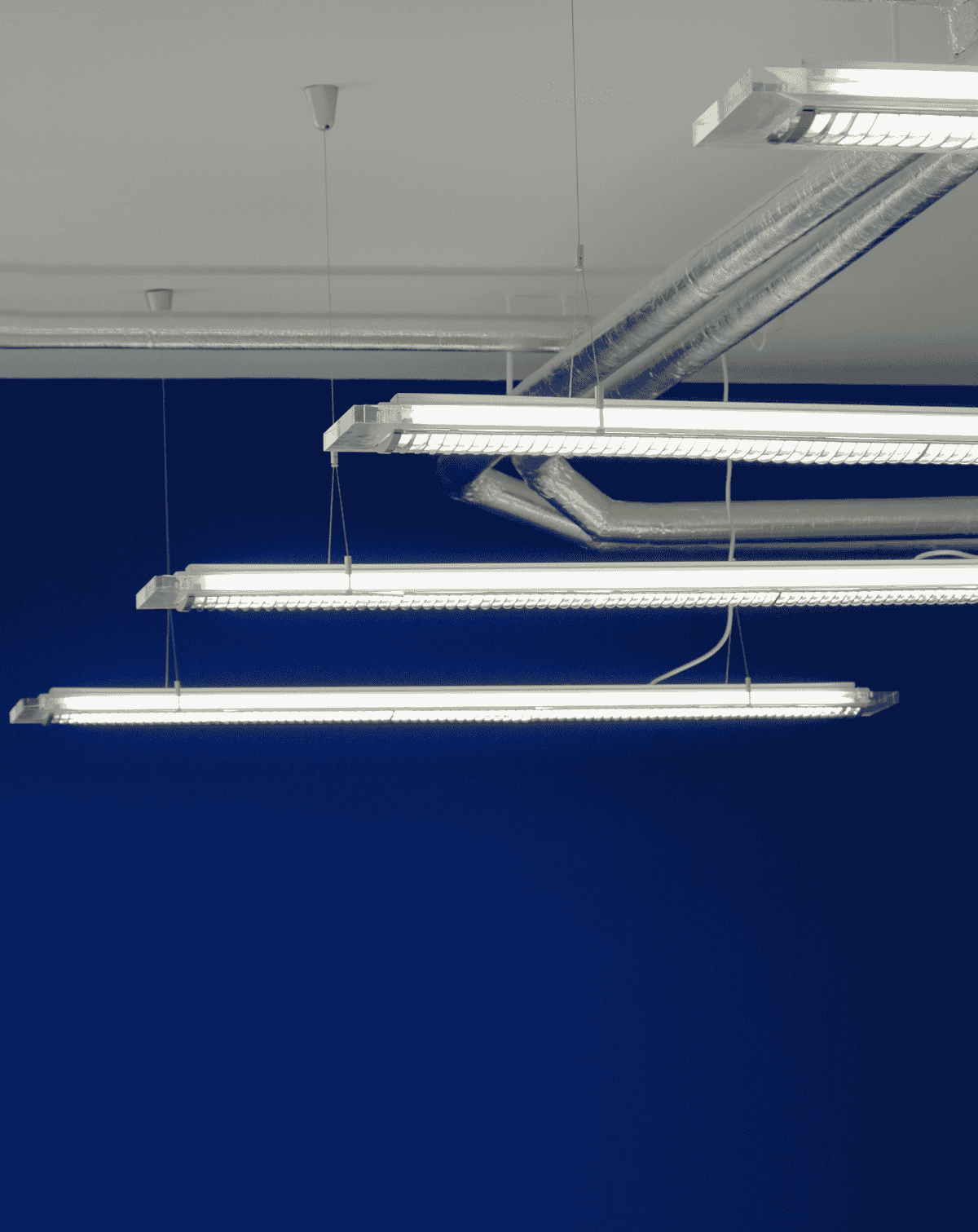 Luminaires suspendus à tubes fluorescents et conduits apparents typiques de l'éclairage industriel.