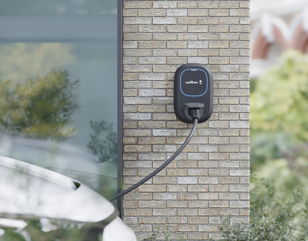 Wallbox domestique fixée sur un mur de briques à côté d'une voiture électrique.